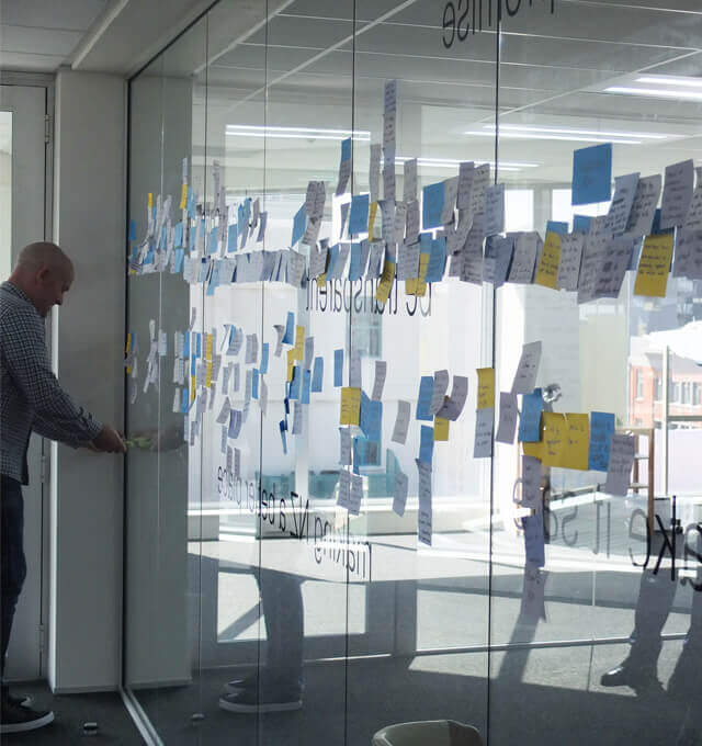 A project discovery workshop facilitator places post-its on a glass wall during user story mapping.